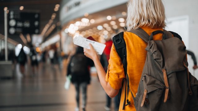 Rear view of a woman at the airport holding a passport with a boarding pass as she walks to her departure gate