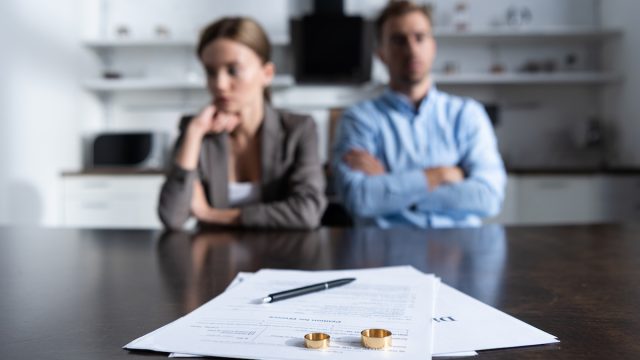 An unhappy couple sitting at a table with divorce documents and their wedding bands.