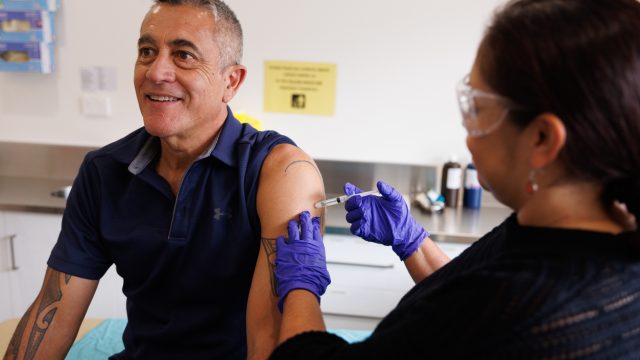 A man receiving a vaccine shot in his arm from a female medical professional