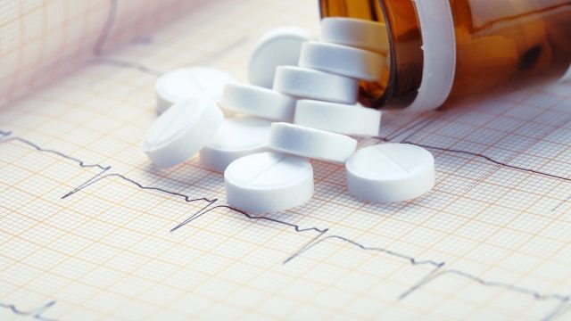 white pills spilling out of the bottle onto an EKG readout