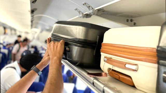 cropped image of a man putting a suitcase in the overhead bin on an airplane