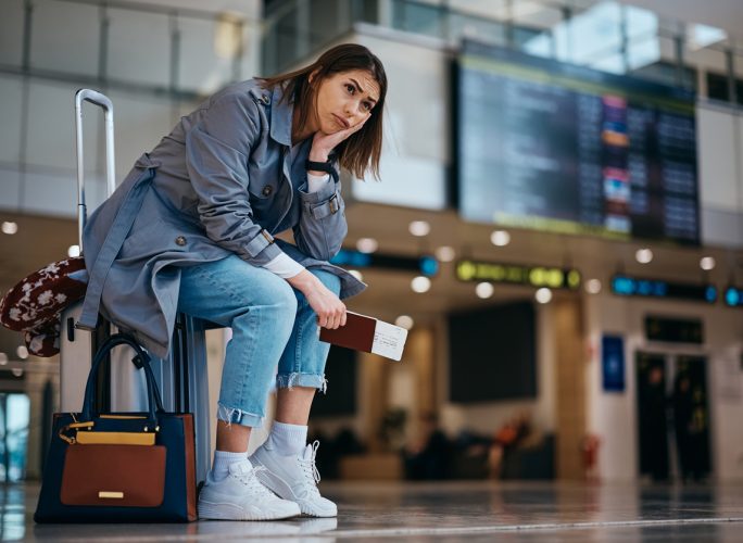 Upset woman sitting on her suitcase after her flight being canceled at the airport.