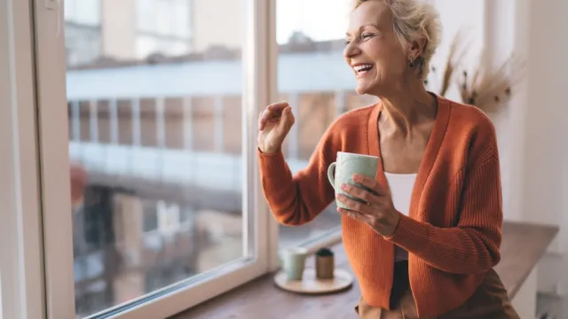 Stylish senior woman laughing wearing orange cardigan with coffee mug