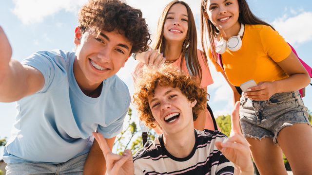 Happy smiling group of teenagers high school pupils friends classmates college students boys and girls with bags hanging out in park nature street outside take selfie shot picture photo having fun