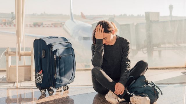 an upset woman sitting on the floor at the airport with her suitcase next to her