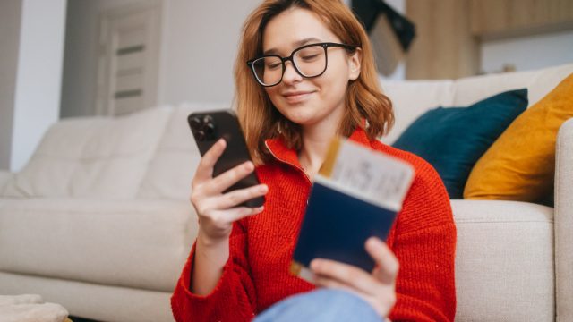 A cheerful woman uses her smartphone to make an online reservation for her holiday trip