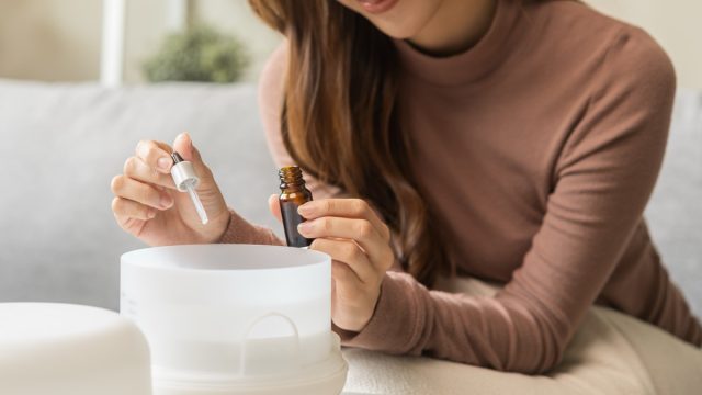Close up of a young woman adding oil to her aromatherapy diffuser while sitting on her couch
